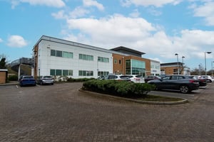 Exterior view of Care Fertility Nottingham clinic, a modern two-storey building with white and brick façades, large windows, and a car park in front under a blue sky.