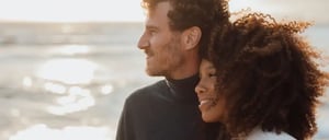 A couple together looking in the distance on the beach with the sea in the background.