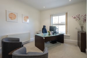 Second consultation room at Care Fertility Tunbridge Wells with armchairs, a glass-topped desk, and fresh flowers