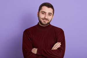 Man smiling confidently with arms crossed against a purple background, conveying warmth and reassurance.
