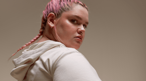Woman with pink hair looking into the camera against a beige background