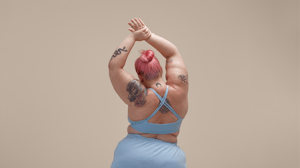 Woman with pink hair and tattoos from behind, wearing blue work out clothes, stretching ready to exercise